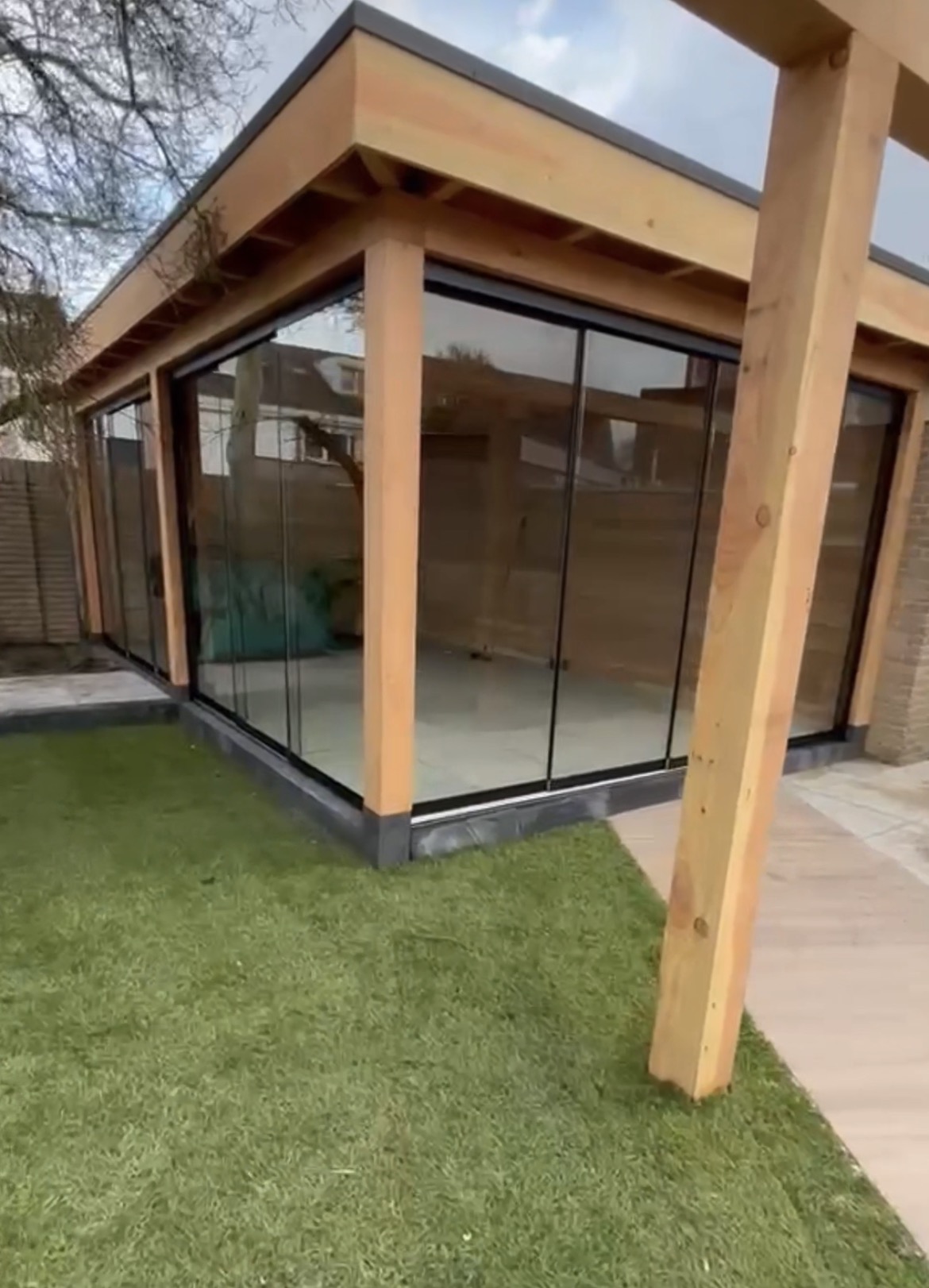 Glazen schuifwanden rondom een houten overkapping met zicht op de tuin