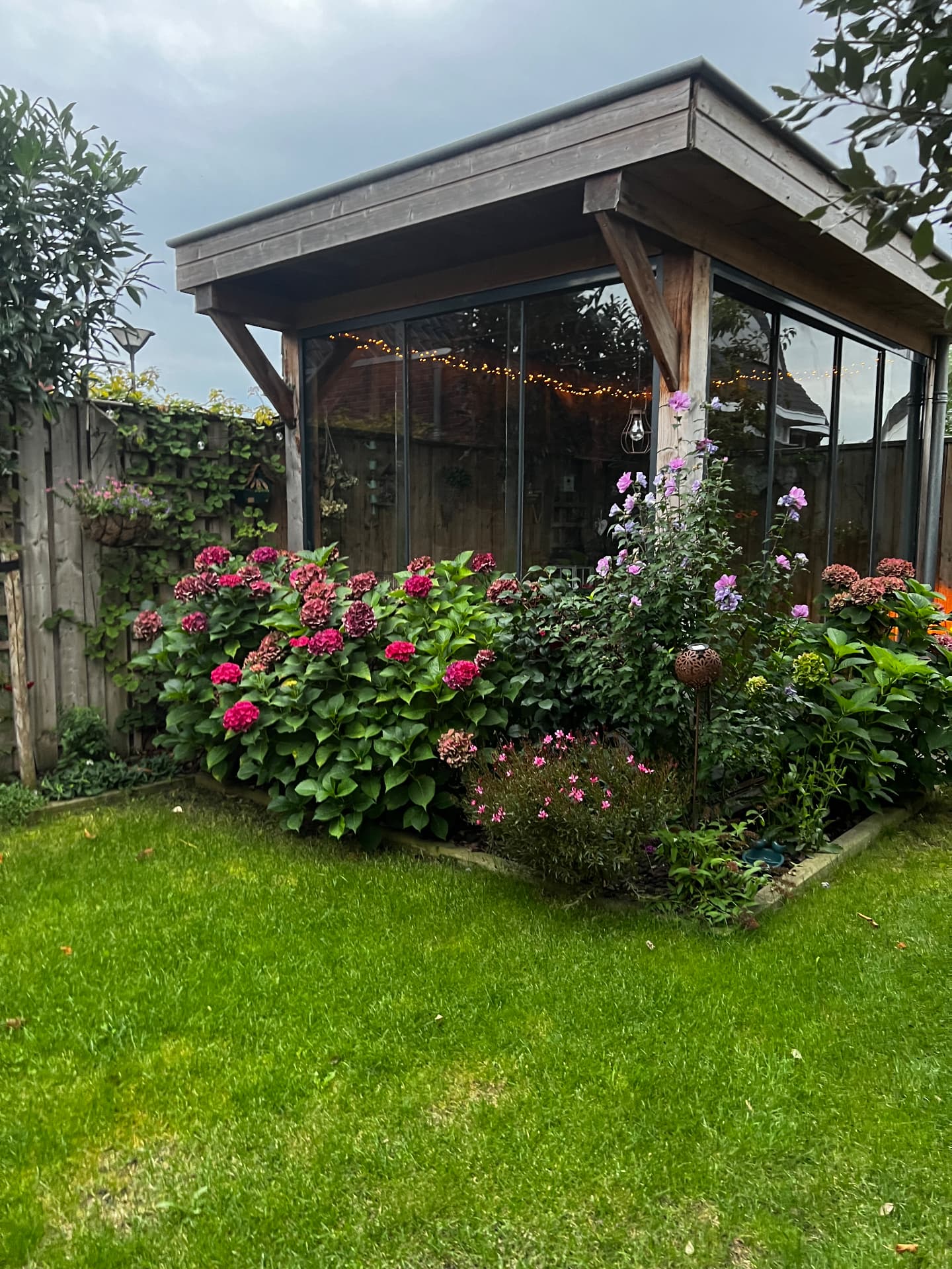 Glazen schuifwanden rondom een houten overkapping met bloementuin