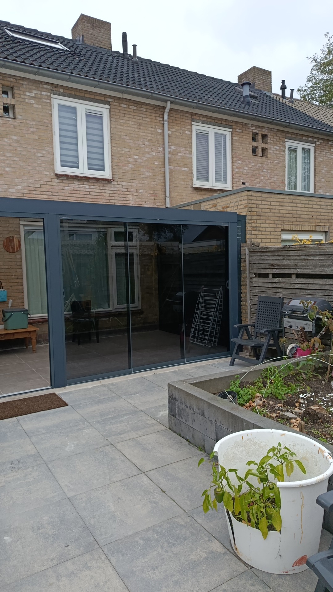 Overkapping met gesloten glazen schuifwand aan de zijkant van een tuin