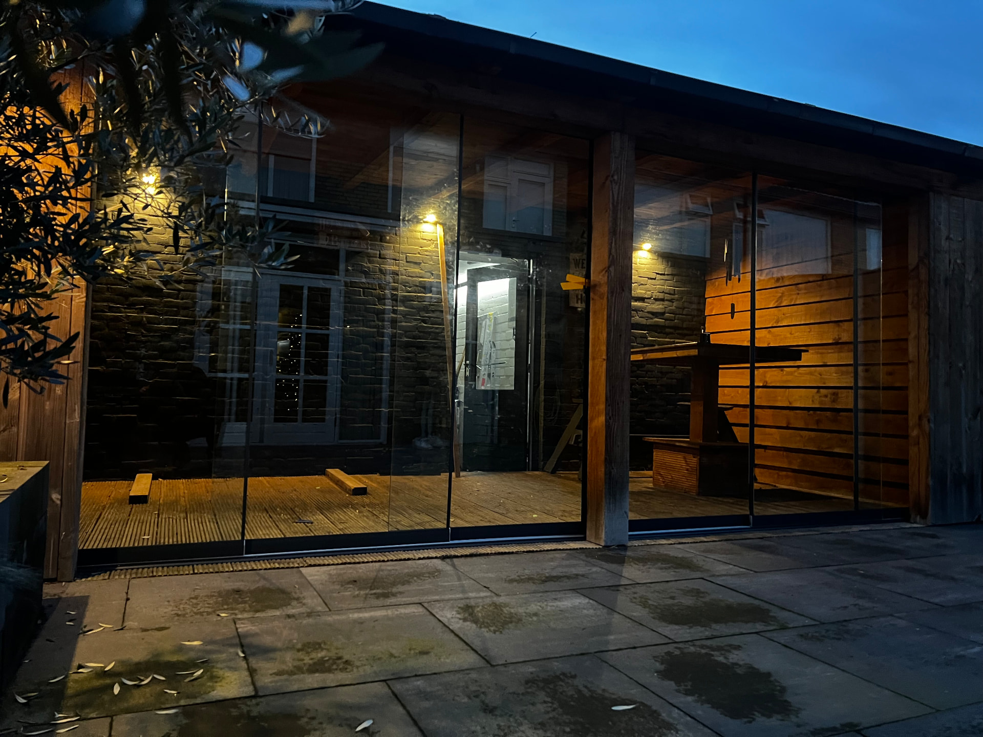 Glazen schuifwand in donker glas bij een houten overkapping in de avond